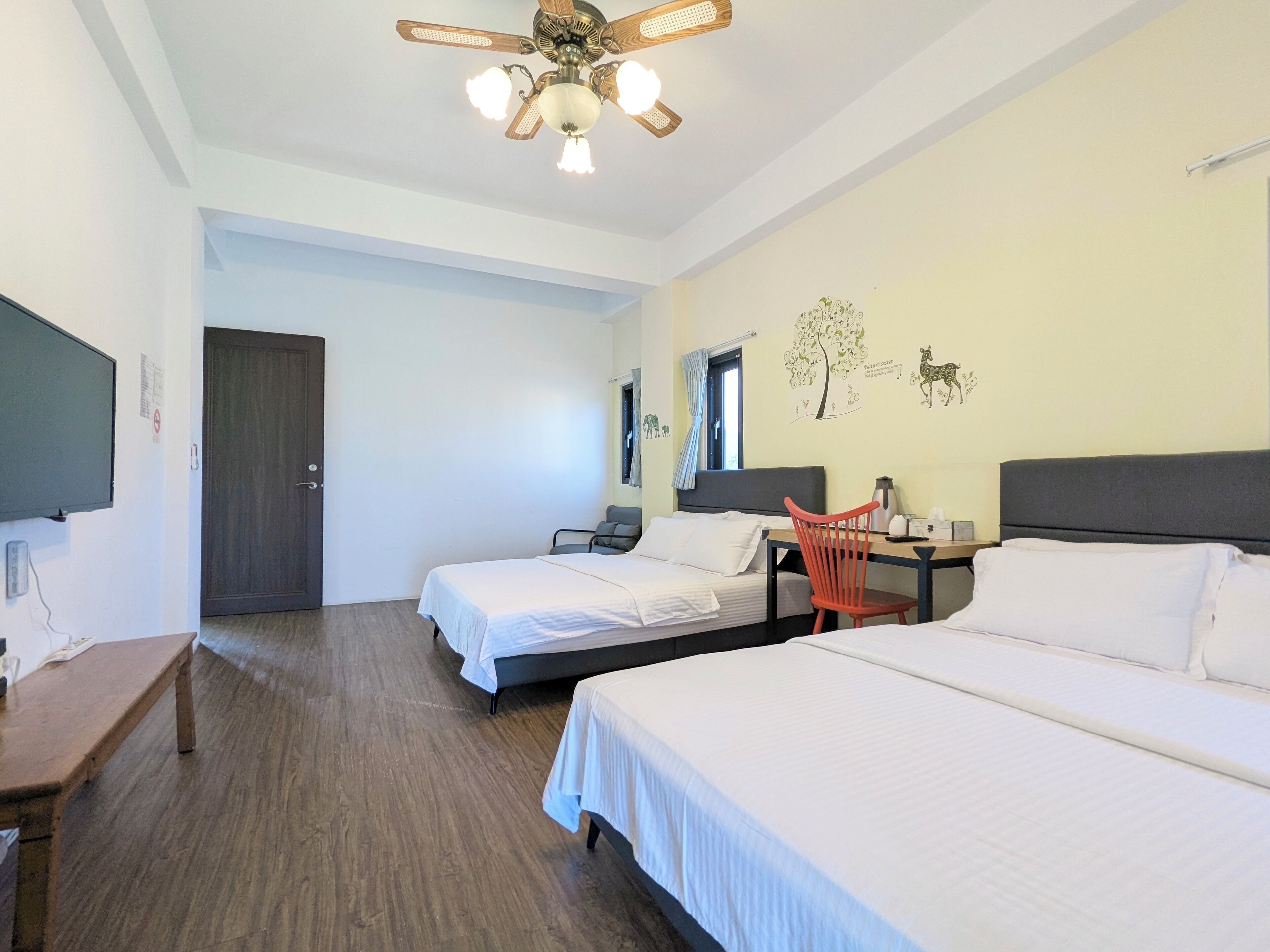 Une chambre d’hôtel avec deux lits, un bureau, une chaise, une télévision et un ventilateur de plafond.
