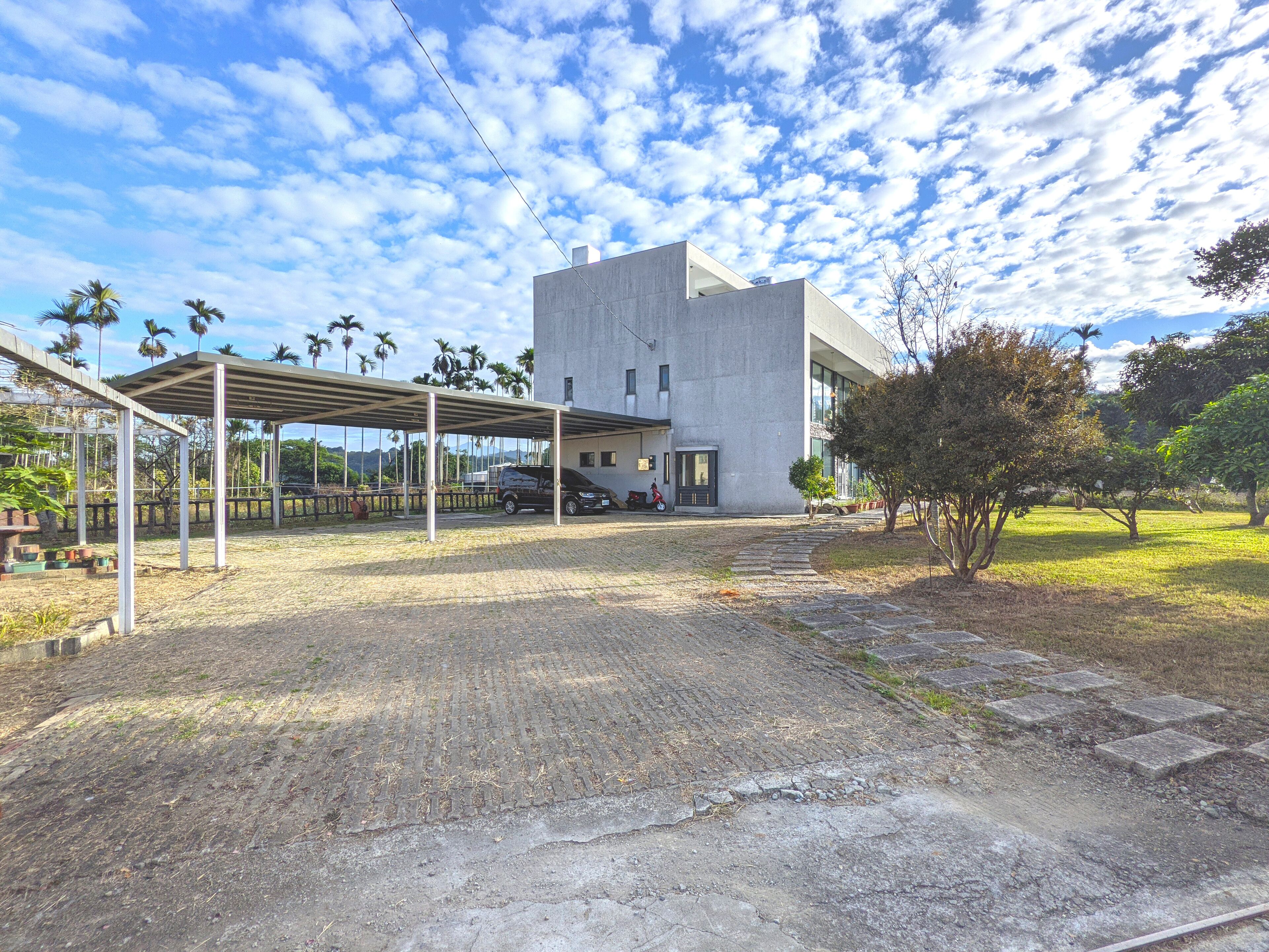 A modern building with a covered parking area, a paved walkway, and a grassy area with trees.