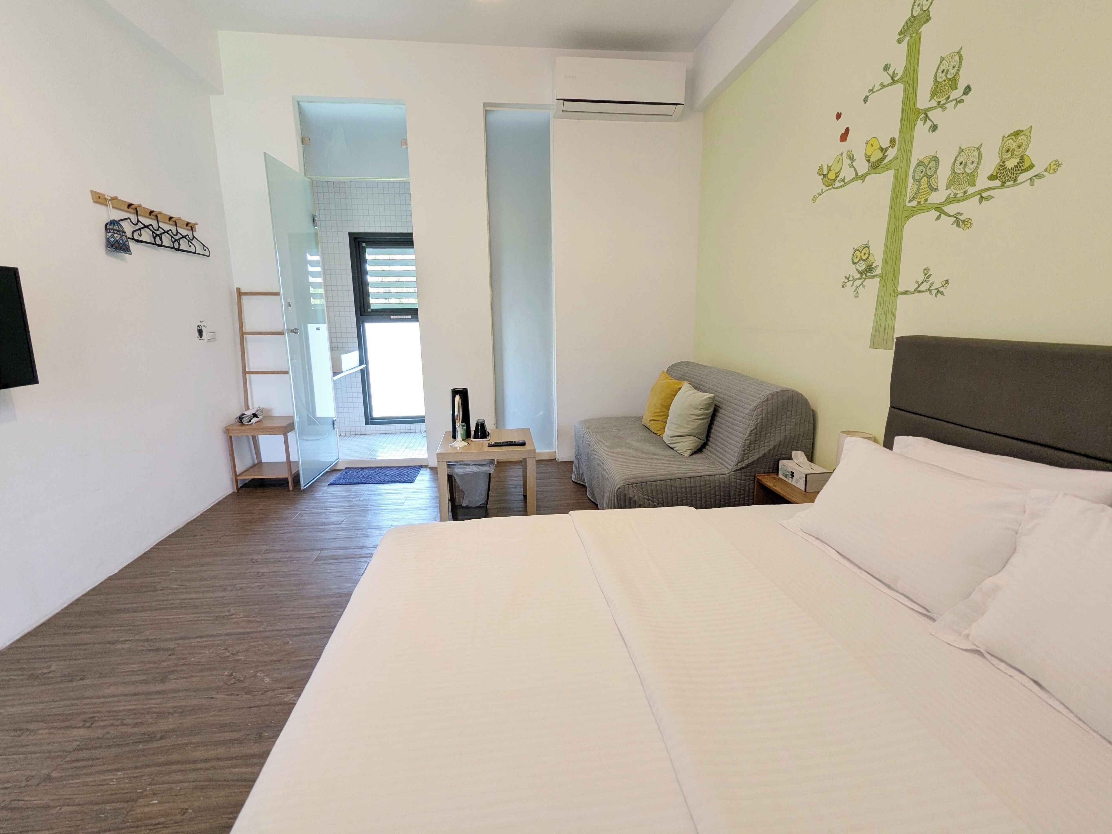 Una habitación de hotel con cama, sofá, escritorio y televisión montada en la pared.