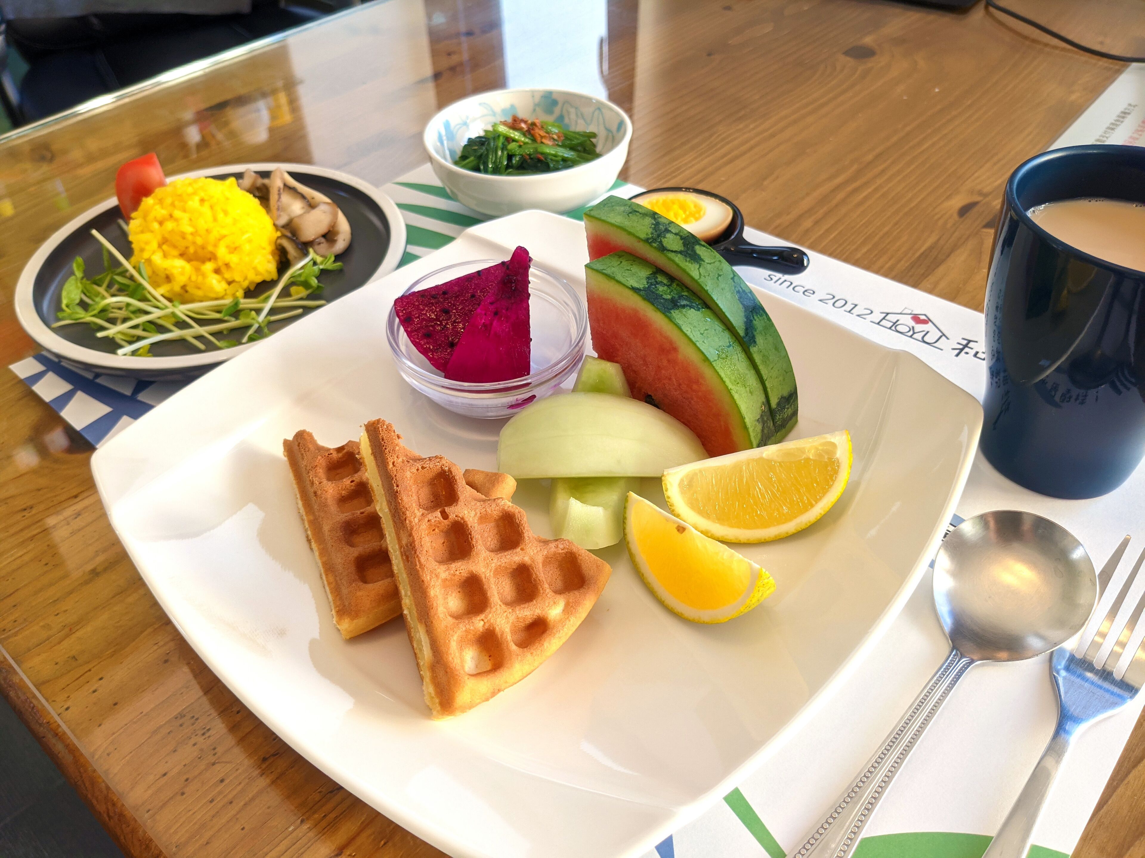A plate with waffles, watermelon, lemon, and a small bowl of dragon fruit.