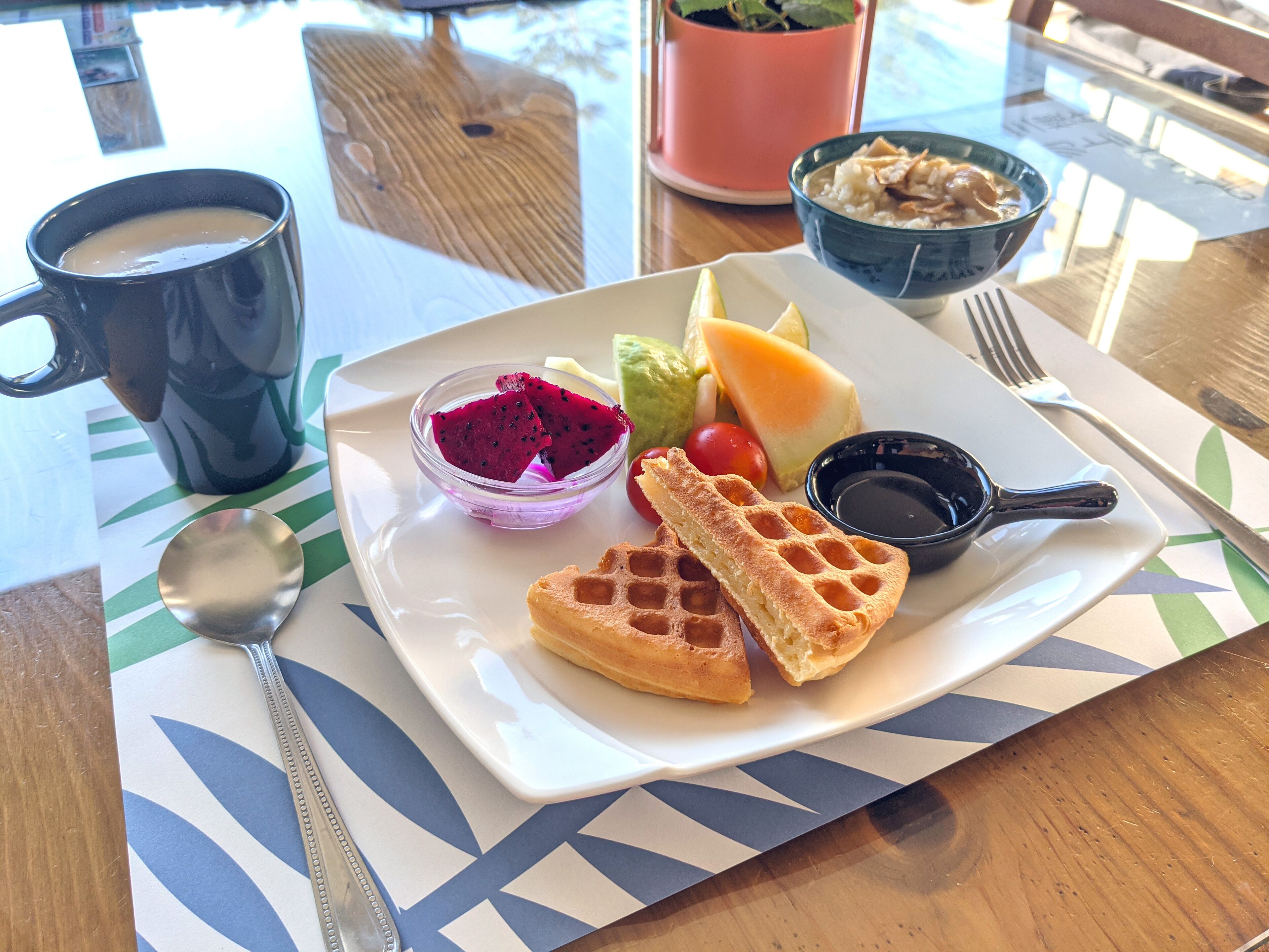 En bakke med morgenmad, vafler, frugt og en kop kaffe på et bord.