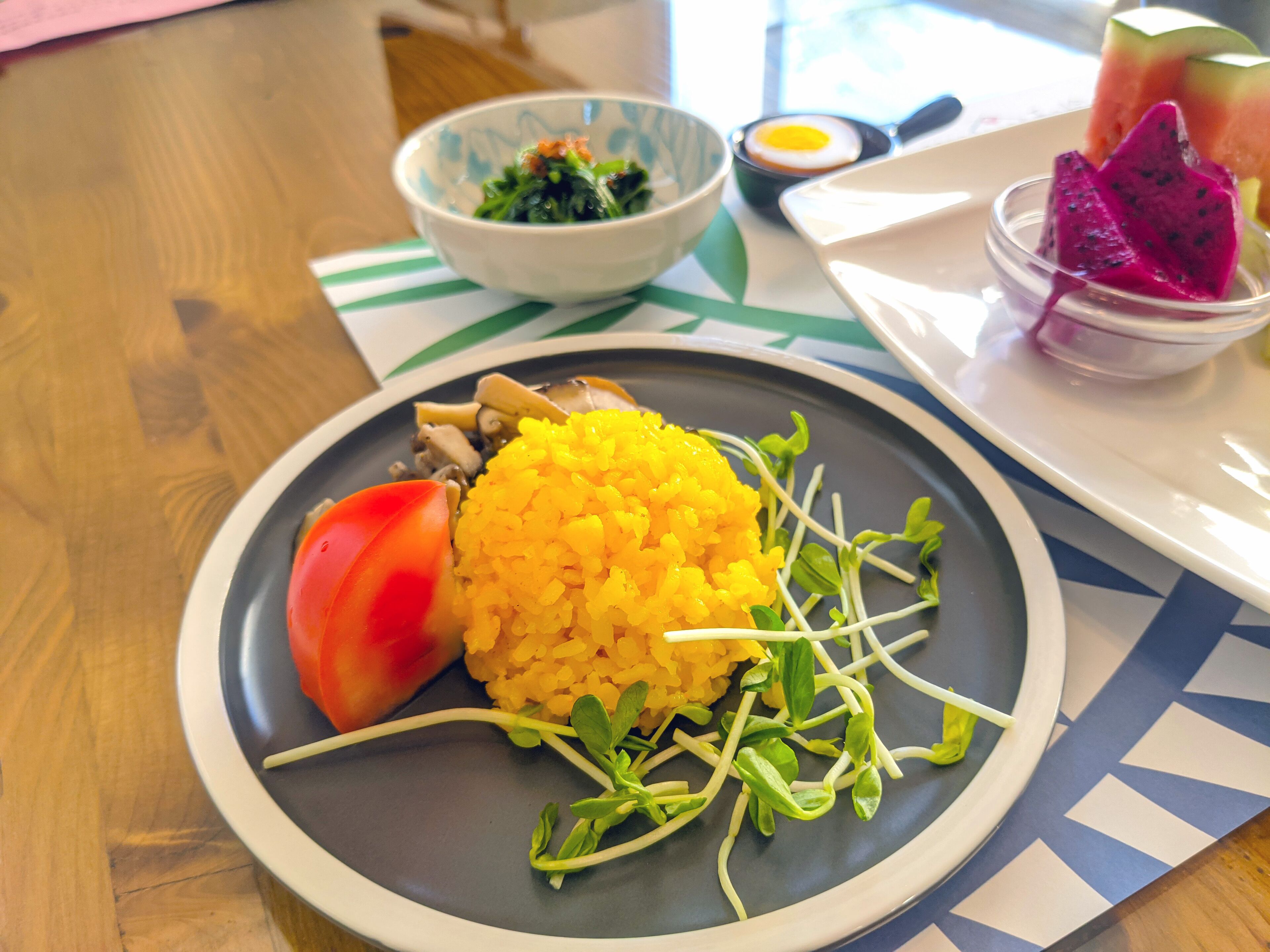 A plate with yellow rice, a slice of tomato, and green sprouts.