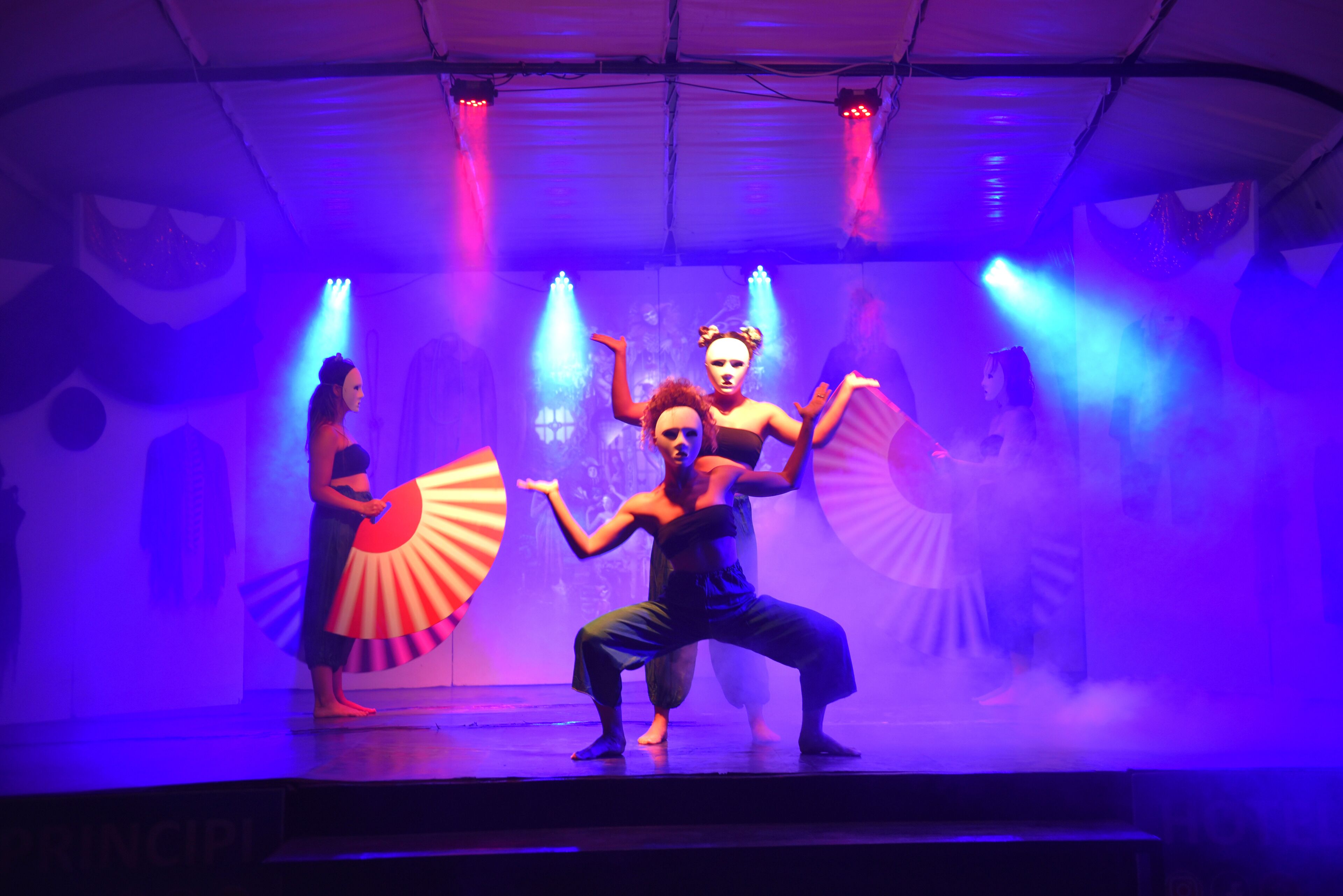 Un escenario con artistas en poses dinámicas, iluminado por luces azules y púrpuras.