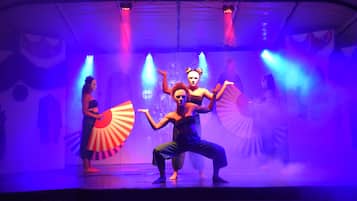 Un escenario con artistas en poses dinámicas, iluminado por luces azules y púrpuras.