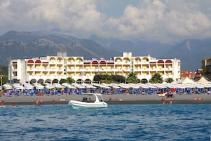 A hotel with multiple balconies, a beach area with umbrellas, and a boat in the water.