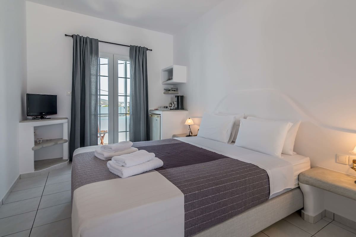 A hotel room with a large bed, a TV, a desk with a lamp, and a view of the outdoors.