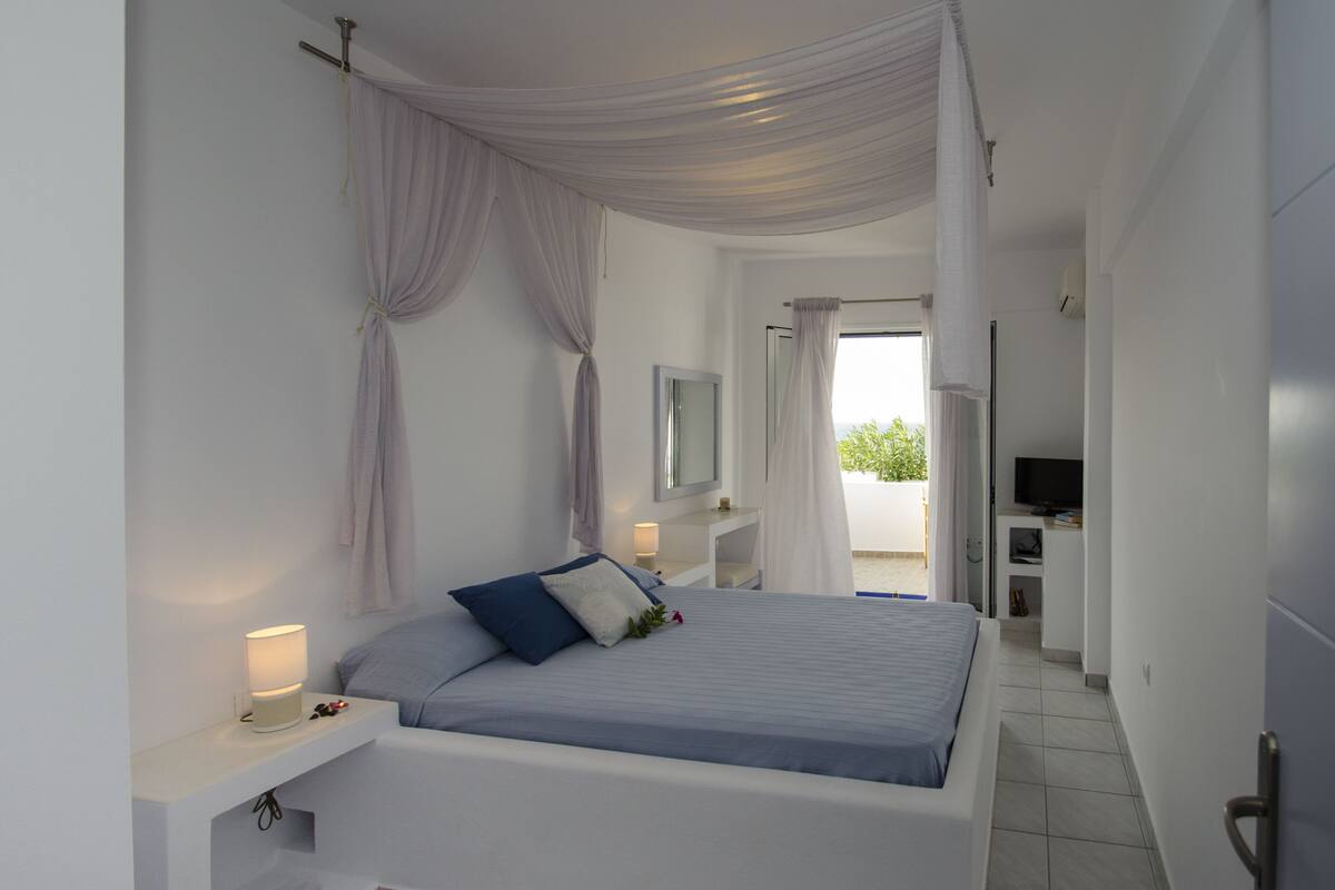 A bedroom with a bed, bedside lamps, a mirror, and a TV.