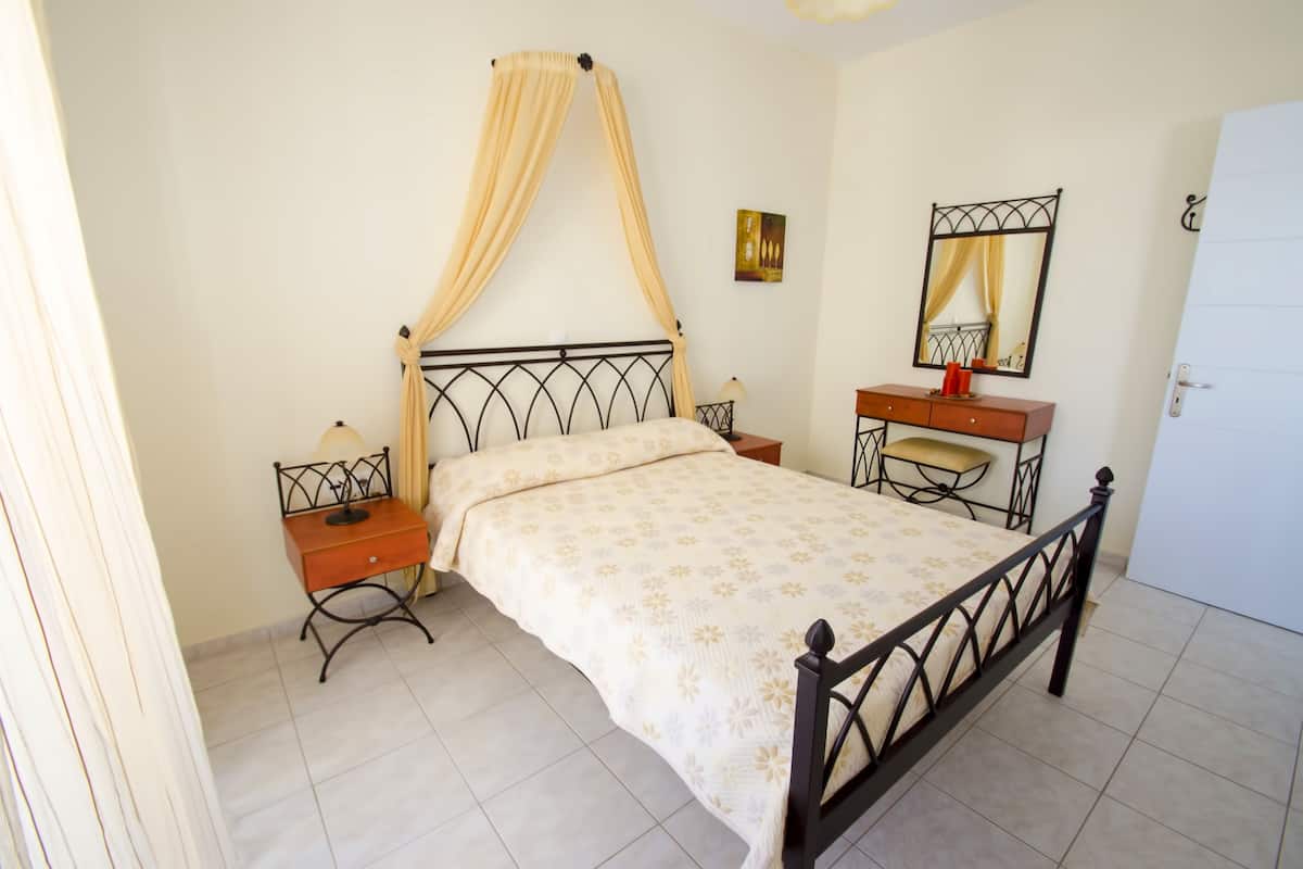 A bedroom with a bed, nightstands, a vanity, and a mirror.