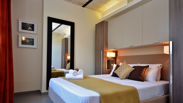 Habitación de hotel con cama, espejo, mesita de noche y lámpara de pared.