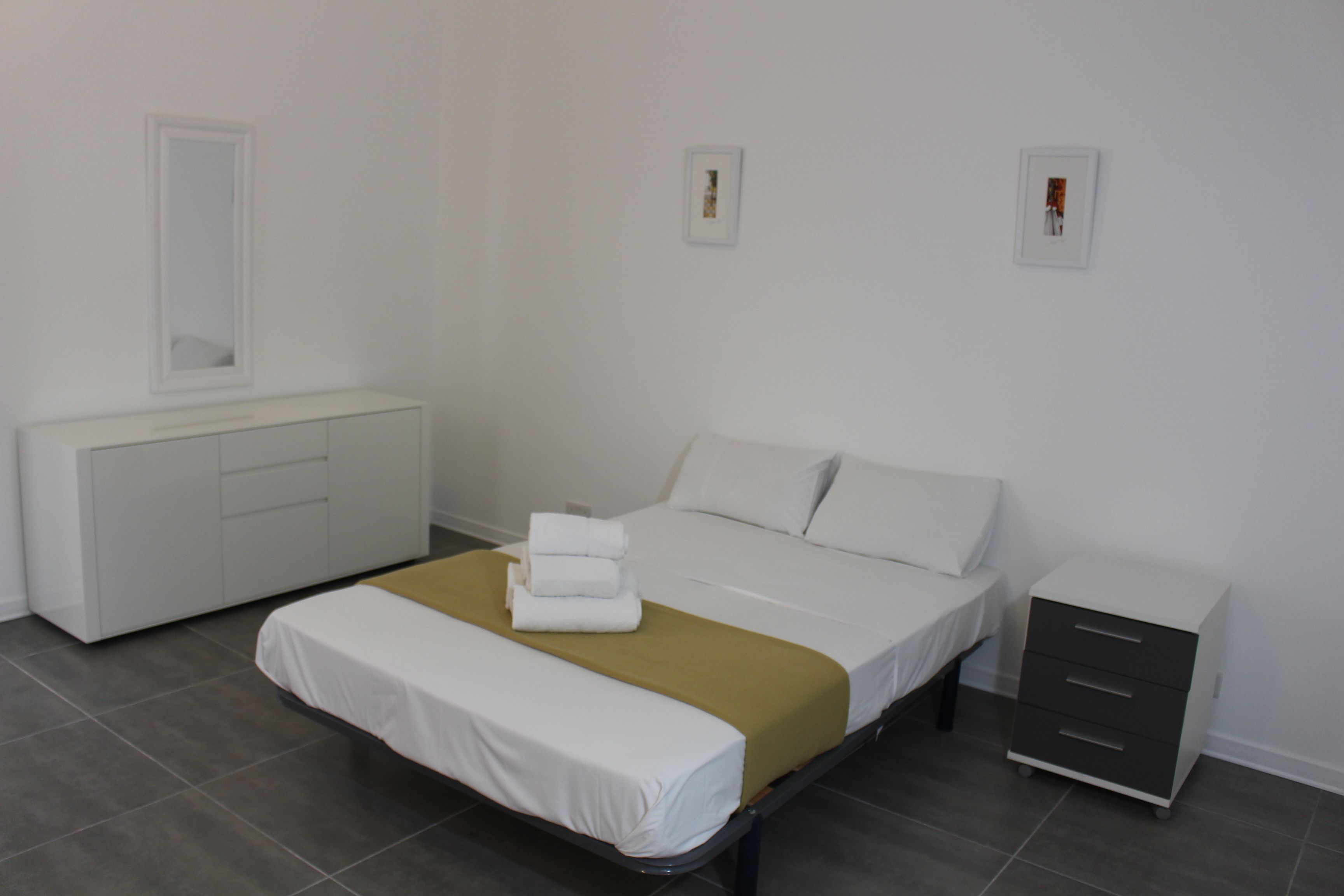 A neatly arranged bedroom with a bed, bedside tables, a wardrobe, and a mirror.