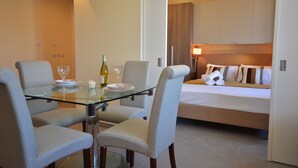 Una habitación de hotel moderna con una mesa de cristal, cuatro sillas, una cama con almohadas y una mesita de noche con lámpara.