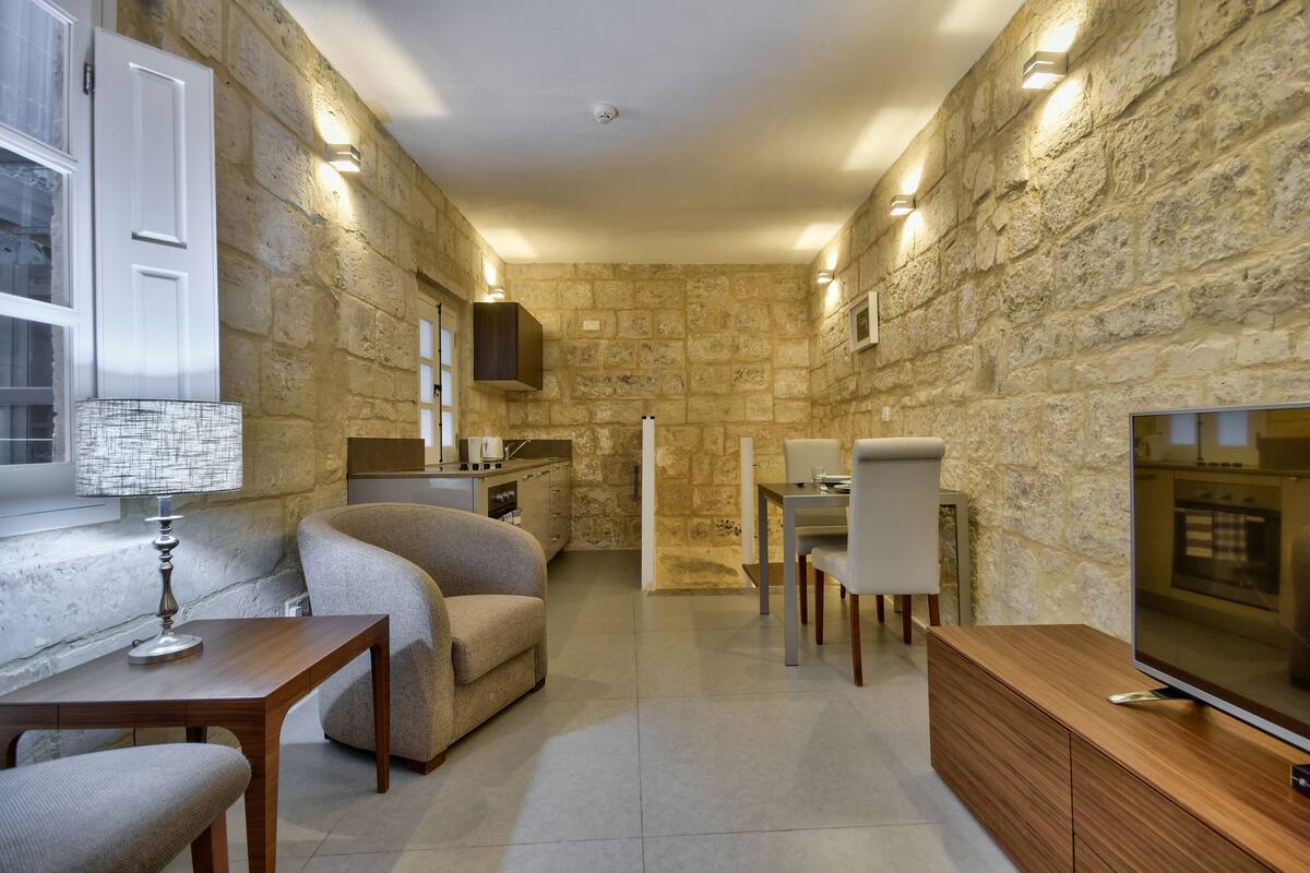 Una sala de estar acogedora con pared de piedra, televisor, sofá y zona de comedor.
