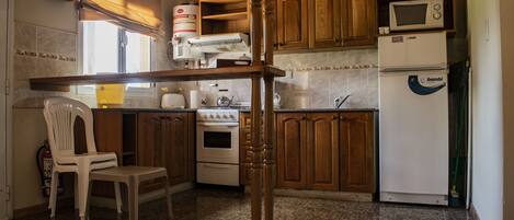 A kitchen with wooden cabinets, a microwave, a refrigerator, a stove, and a chair.