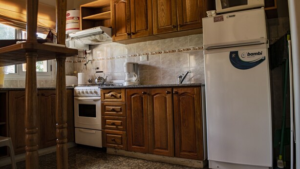 A kitchen with wooden cabinets, a stove, a microwave, and a refrigerator. - Complejo las Calandrias (Sierra de la Ventana)