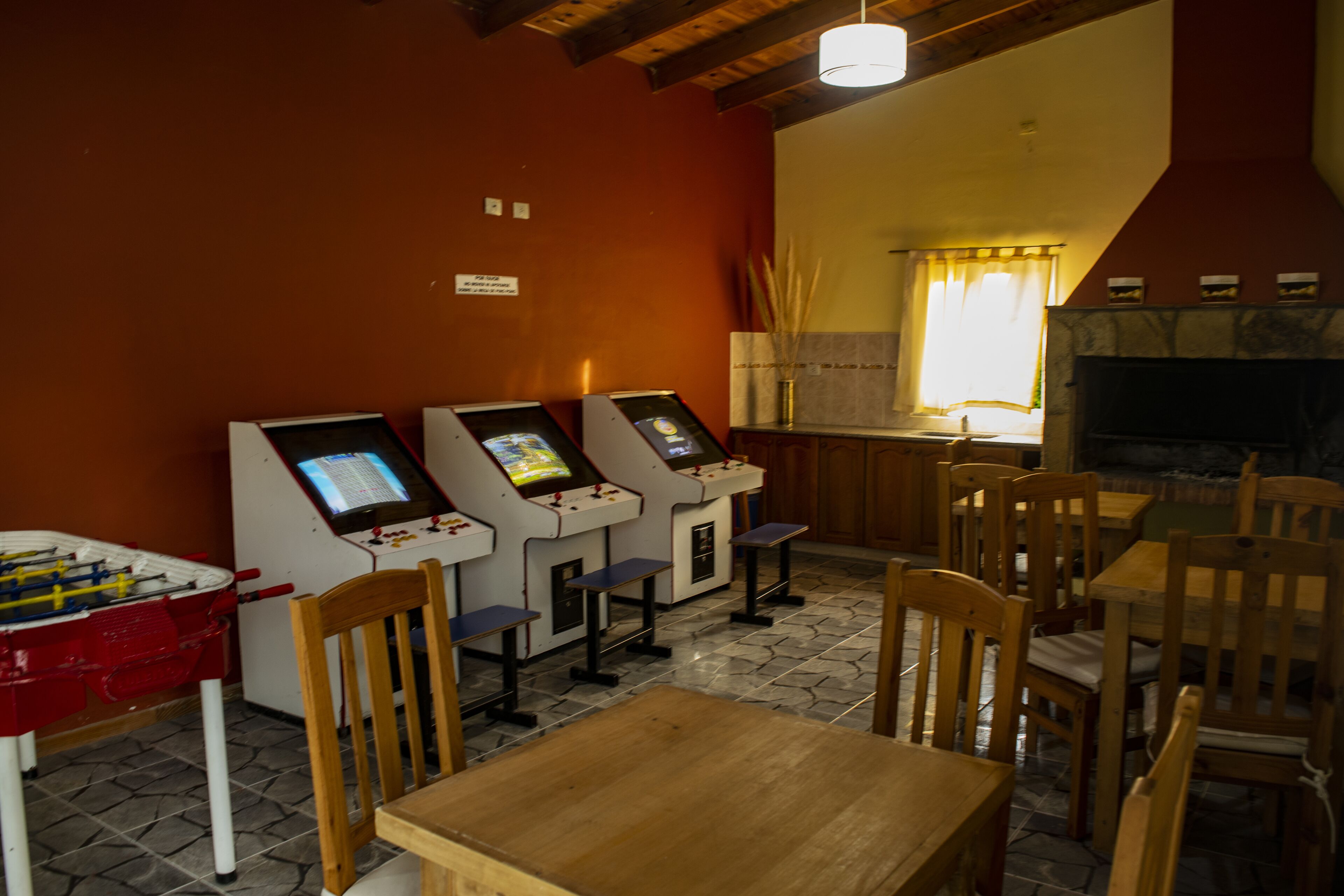 A restaurant with wooden tables and chairs, a foosball table, and three self-service kiosks.