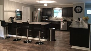 A modern kitchen with a central island, bar stools, stainless steel appliances, and a clock on the wall. - Whitewater Condos (Canyon Lake)