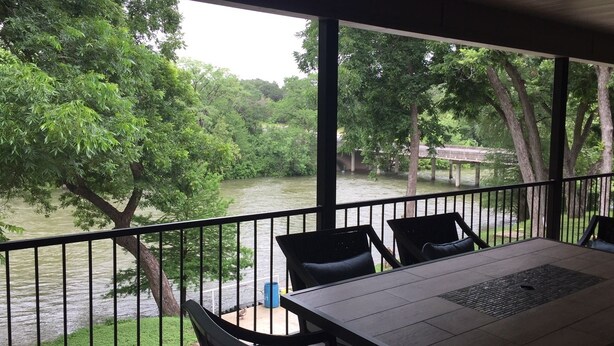 A covered outdoor area with a table and chairs, overlooking a river and lush greenery. - Whitewater Condos (Canyon Lake)