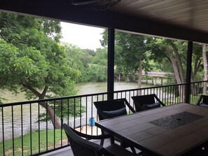 A covered outdoor area with a table and chairs, overlooking a river and lush greenery. - Whitewater Condos (Canyon Lake)