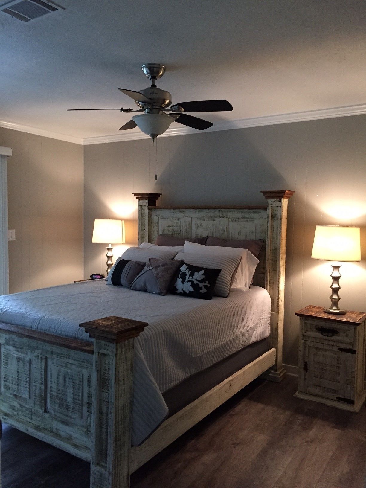 Une chambre avec un lit en bois, un ventilateur de plafond et deux tables de chevet avec des lampes.