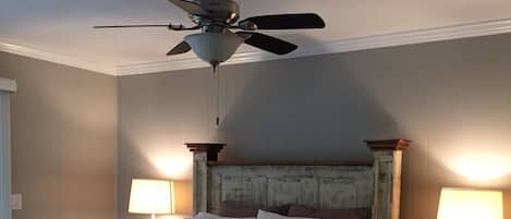 Une chambre avec un lit en bois, un ventilateur de plafond et deux tables de chevet avec des lampes.
