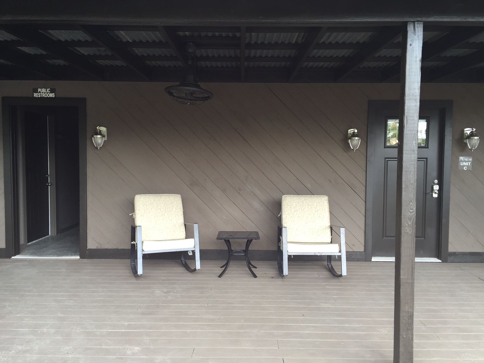 A covered outdoor seating area with two chairs and a small table, a sign for public restrooms, and a door labeled "UNIT C".