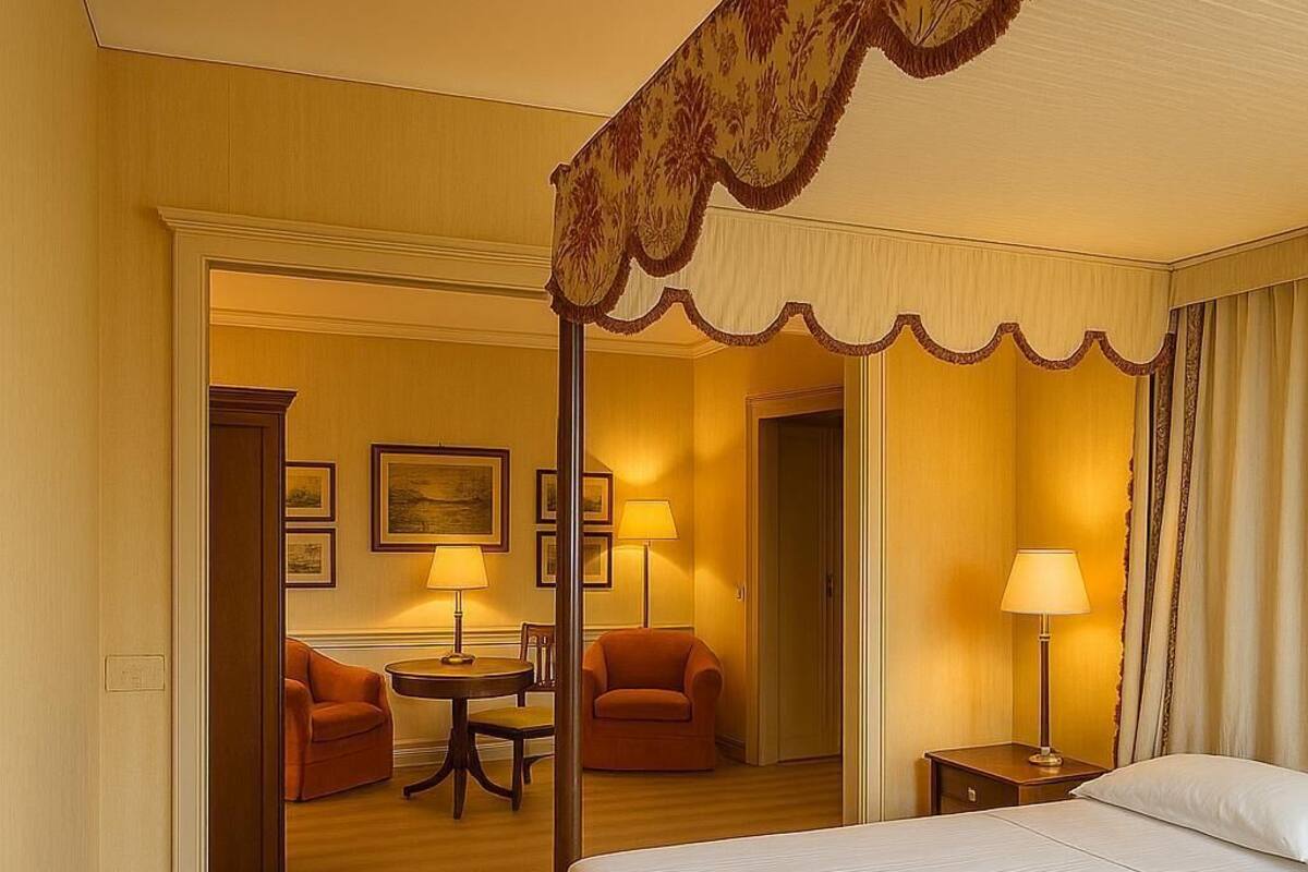 A hotel room with a four-poster bed, a sitting area with a table and chairs, and a separate bedroom with a single bed.