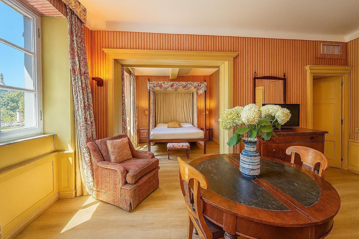 A room with a bed, a sitting area with a chair and a table, and a television.