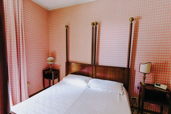 A neatly made bed in a room with checkered wallpaper, a wooden headboard, and two bedside tables with lamps. - Resort Dei Limoni (Lucca)