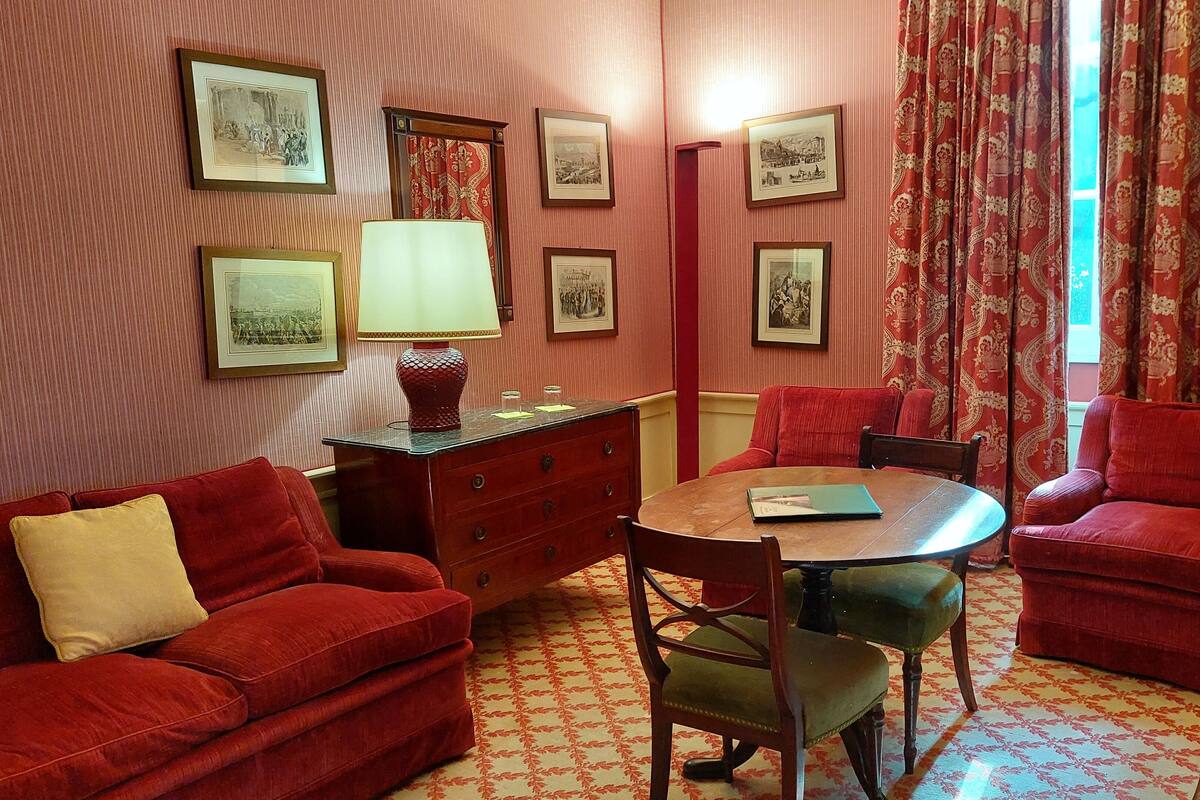 A room with a red sofa, a wooden table, and chairs, a dresser, and framed pictures on the wall.