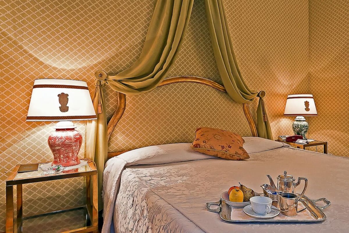 A neatly made bed with a tray of tea and pastries, two bedside lamps, and a mirror on the wall.