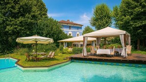 A swimming pool with lounge chairs and umbrellas, surrounded by lush greenery and a building in the background. - Resort Dei Limoni (Lucca)