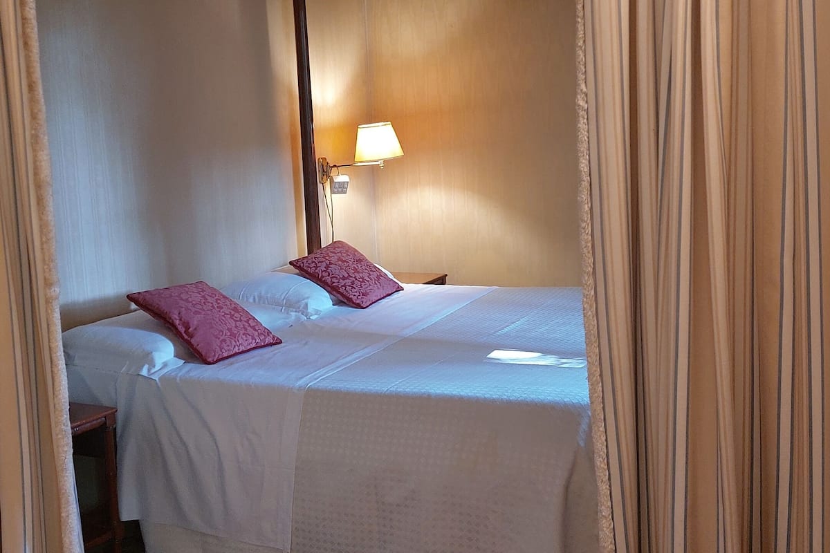 A single bed with a canopy, a bedside table, a lamp, and a floral-patterned carpet.