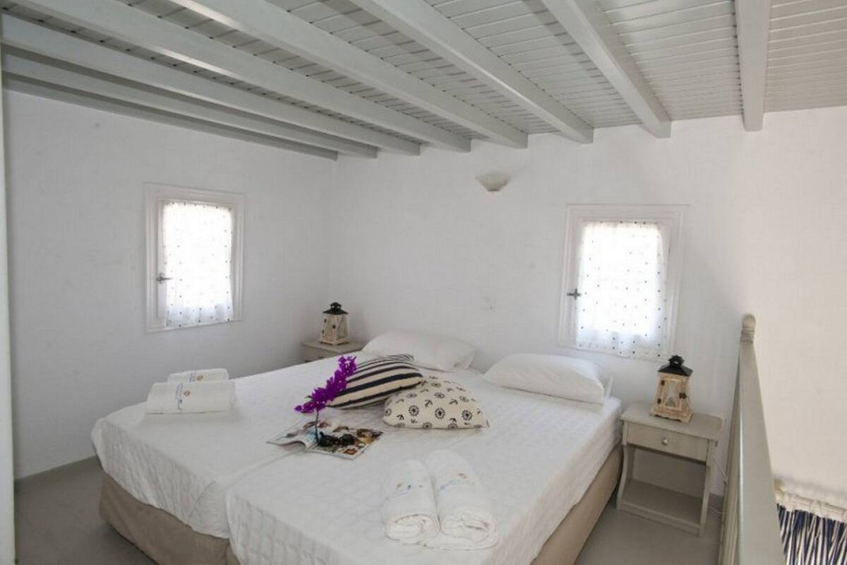 A white room with a bed, two nightstands, and two windows.