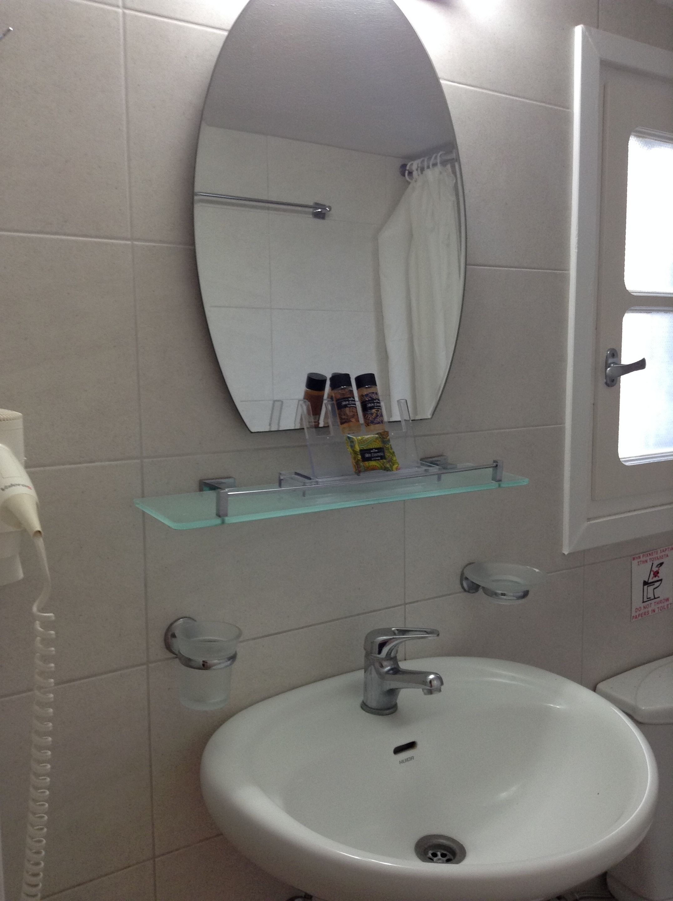 A bathroom with a white sink, a mirror, and a glass shelf with toiletries.