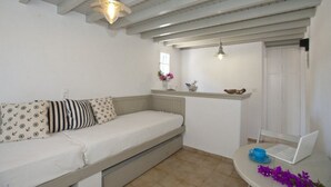 A compact room with a sofa, a small table with a laptop, and a shelf with decorative items. - Gryparis Club Apartments (Mykonos)