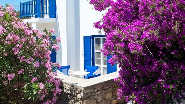 A white building with blue shutters and balconies, surrounded by pink bougainvillea. - Gryparis Club Apartments (Mykonos)