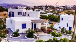 A coastal village with white buildings and blue accents, featuring a paved road and landscaped gardens. - Gryparis Club Apartments (Mykonos)