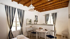 A room with a bed, a desk, two chairs, a small table, and a window with curtains. - Gryparis Club Apartments (Mykonos)