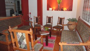Una sala de estar acogedora con muebles de madera, un tapete estampado y un jarrón con flores sobre una estantería.