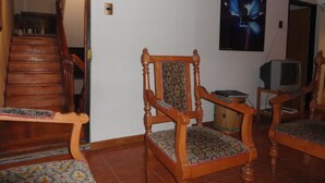 Una sala de estar con una escalera de madera, una silla de madera con un cojín estampado y un televisor sobre un mueble de madera.