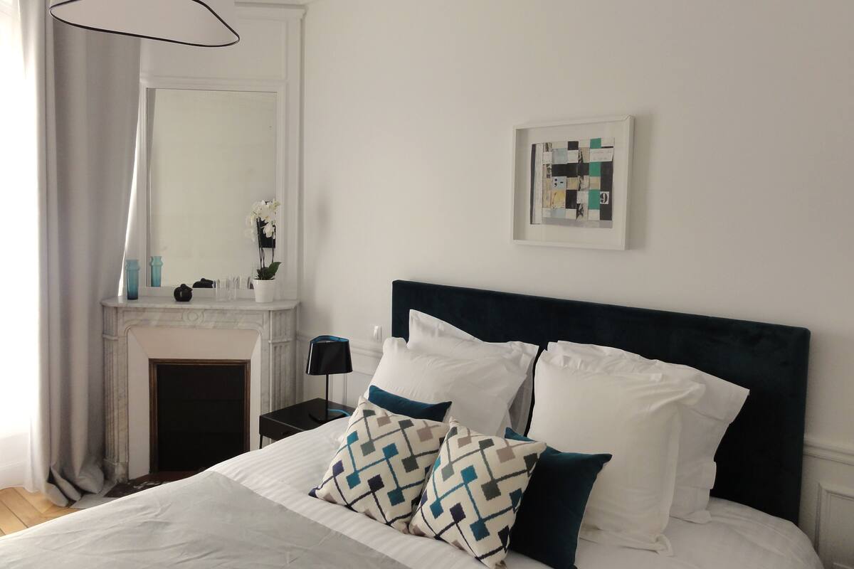 A neatly arranged bedroom with a bed, a nightstand, a mirror, and a framed artwork on the wall.