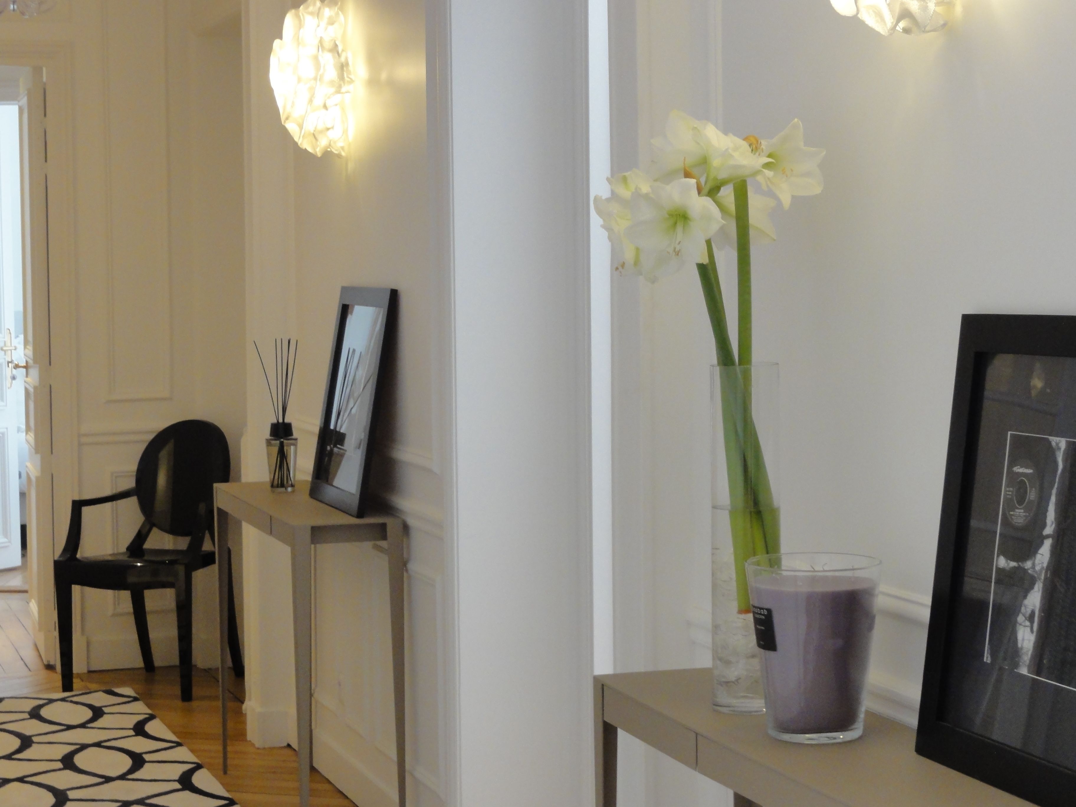 A hallway with a mirror, a framed picture, a vase with flowers, and a candle on a table.