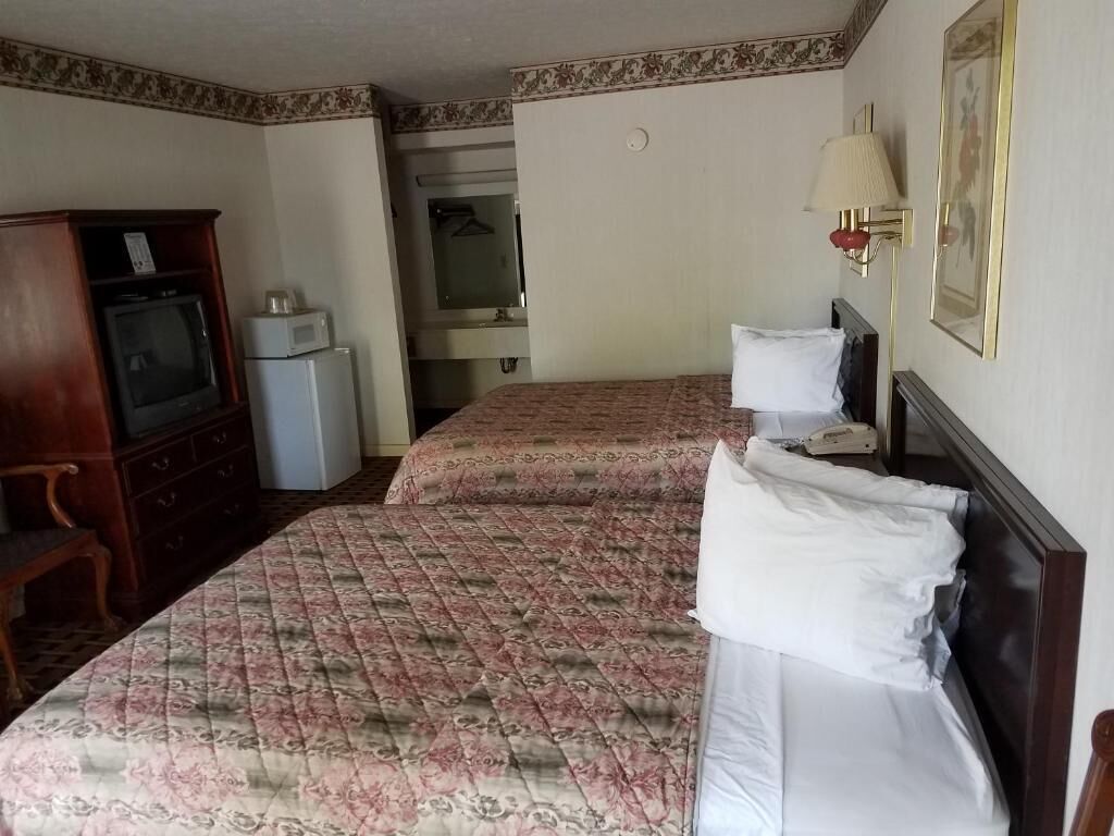 A hotel room with two beds, a wooden dresser, a microwave, and a television.