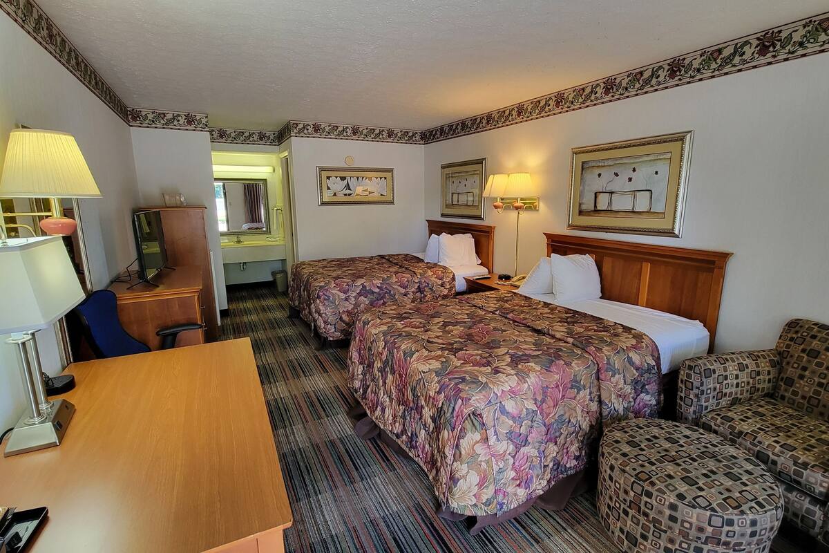 A hotel room with two beds, a desk, a chair, a sofa, and a patterned wall border.