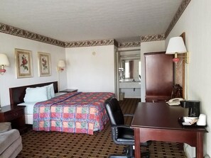 A hotel room with a bed, desk, chair, and a mirror. There are two lamps, a telephone, and a coffee maker on the desk.