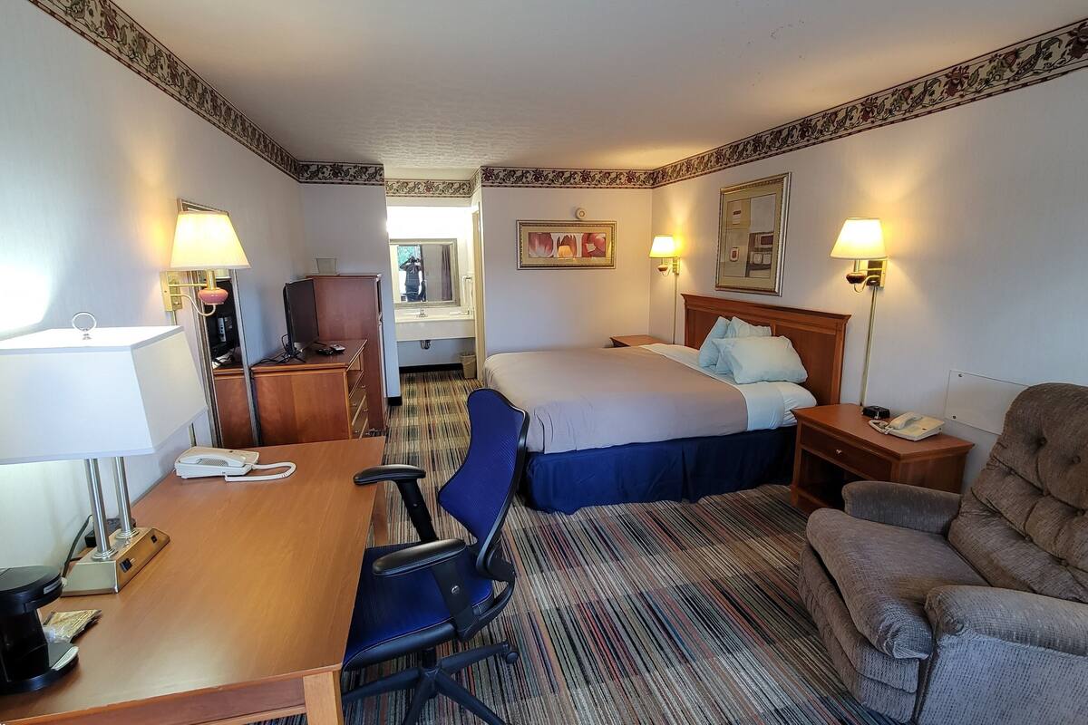A hotel room with a bed, desk, chair, and a television.