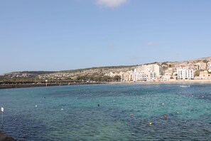 Un pueblo costero con edificios a lo largo del paseo marítimo, agua azul cristalina y un barco a lo lejos.