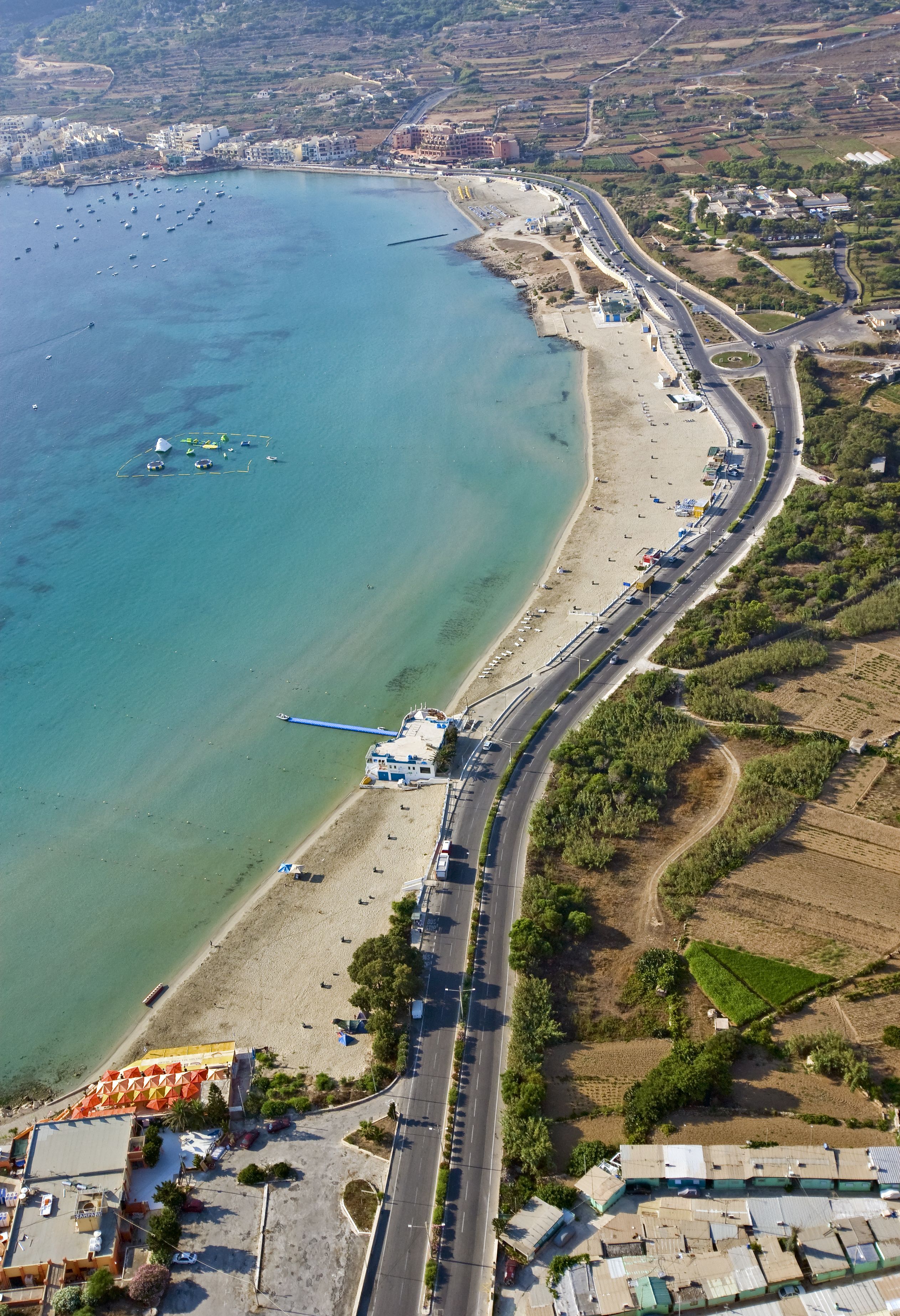 An aerial view of a coastal area with a beach, a road, and buildings.