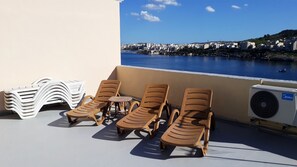Terraza en la azotea con sillones de descanso, una mesa y vistas a una ciudad costera.