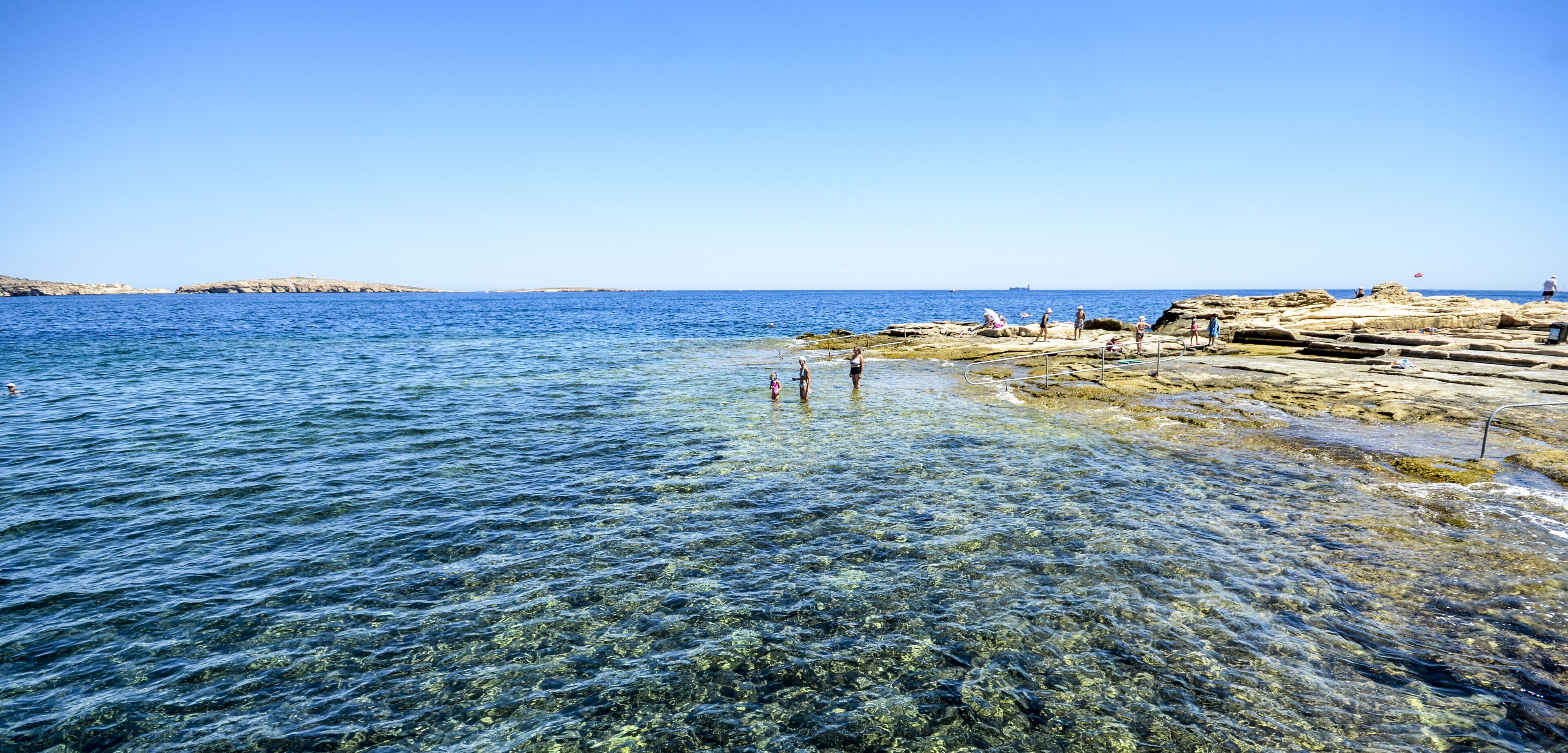 Un rivage rocheux bordé d’une eau claire, où les gens profitent de la plage.